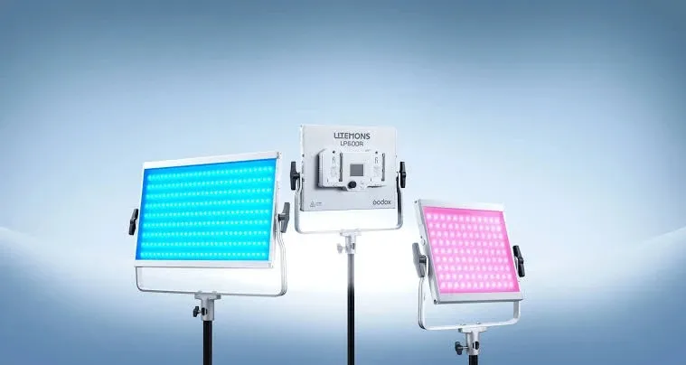 Три LED-панелі Godox Litemons LP600R на стійках на синьому фоні, ліва світить блакитним світлом, центральна повернена задньою панеллю з двома слотами для акумуляторів, права світить рожевим кольором
